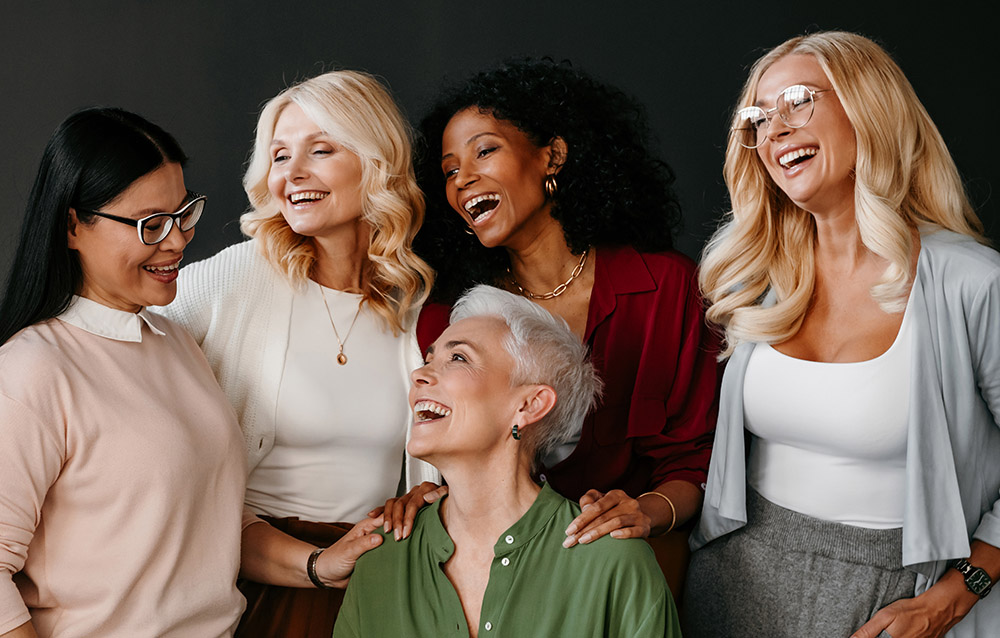 Multi-ethnic group of beautiful mature women bonding and smiling against black background
